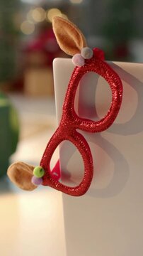 Vertical video: Panning camera showing red glitter glasses on edge at tabletop, focusing green gift
