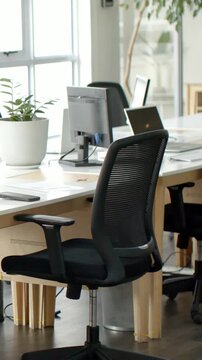 Vertical video: Shifting camera showing black mesh chair at wood desk, revealing laptop and phone