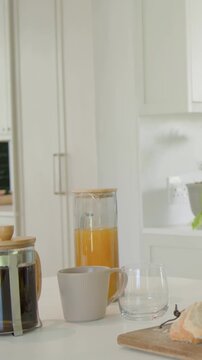 Vertical video: Entering man in blue tee pouring from carafe at island for breakfast, copy space