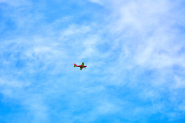 Fototapeta premium Small red airplane flying in clear blue sky with white clouds