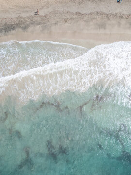 Aerial view of turquoise ocean waves crashing on a sandy beach with a person walking along the shore Santa Maria, Sal, Cabo Verde.