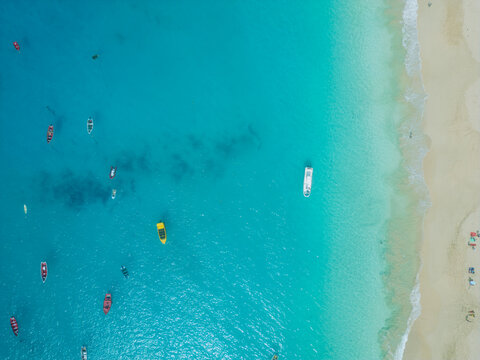 Aerial view of turquoise ocean water and sandy beach with several small boats anchored near the shore in Santa Maria, Sal, Cabo Verde.
