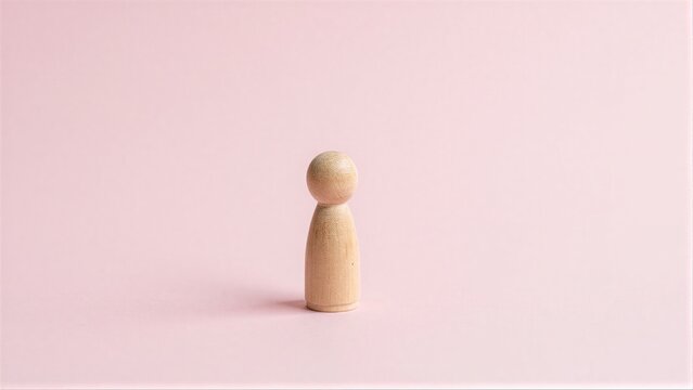 Wooden figure stands alone on soft pink background, minimalist and serene.