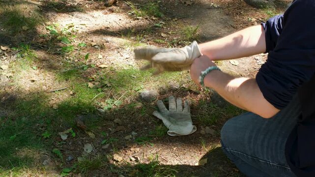 Man kneeling outdoors pulling on heavy duty leather work gloves