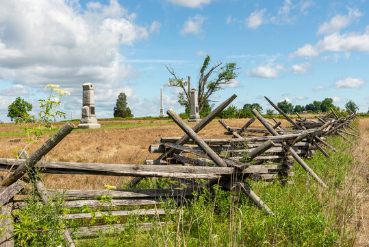 Split rail fences across green fields at Gettysburg National Military Park in Gettysburg, Pennsylvania, USA, under blue sky with clouds.