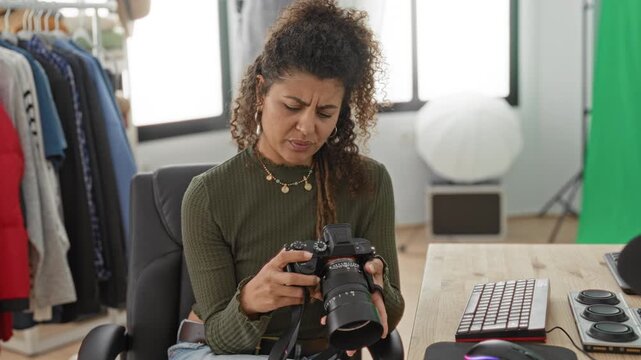 Woman photographer inspects dslr controls, holding camera with furrowed brow and adjusting lens in studio; technical frustration.