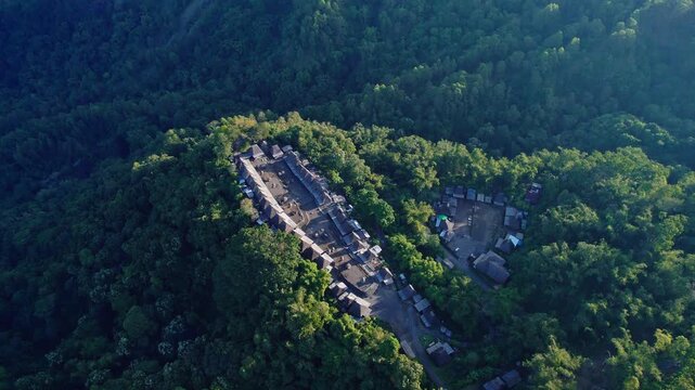 Aerial view of Bena Traditional Village with its iconic thatched roof houses surrounded by lush green forest in Kecamatan Jerebuu, Nusa Tenggara Timur, Indonesia.