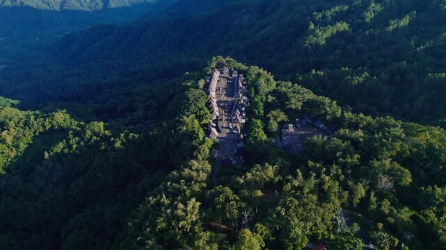 Aerial view of Bena Traditional Village with its iconic thatched roof houses nestled on a lush green mountain ridge in Kecamatan Jerebuu, Nusa Tenggara Timur, Indonesia.