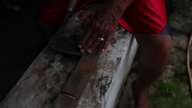 A man sharpens a machete manually with a sharpening stone in a rural village environment. Close-up footage showing traditional tool maintenance, agricultural preparation, and skilled handwork.