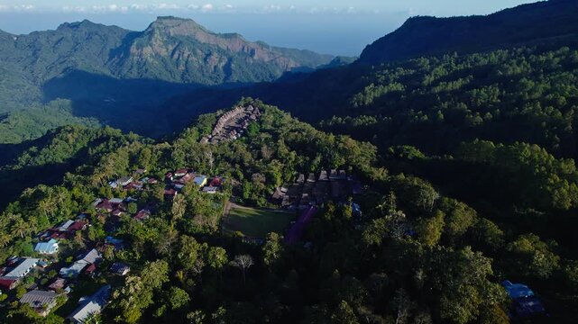 Aerial view of Bena Traditional Village with its iconic thatched roofs nestled among lush green forests and mountains in Kecamatan Jerebuu, Nusa Tenggara Timur, Indonesia.