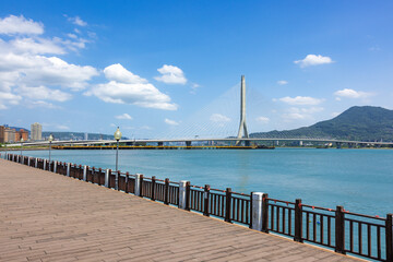 Fototapeta premium Wooden seaside walkway overlooking modern Danjiang Bridge in Tamsui Taiwan