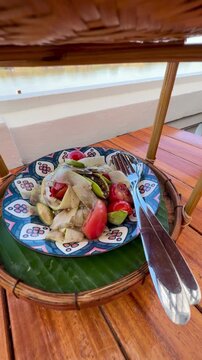 Close-up of authentic Thai spicy papaya salad or call Somtum and crispy pork cracklings platter set on wooden table by river