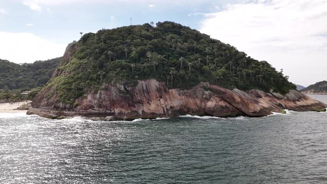 Aerial view of the lush Morro do Leme hill with rocky cliffs and waves crashing against the shore in Rio de Janeiro, State of Rio de Janeiro, Brazil.