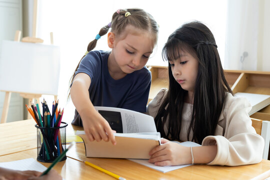 Elementary school students reading and studying together in classroom. Diverse children collaborating on schoolwork, peer learning, teamwork, and education concept.