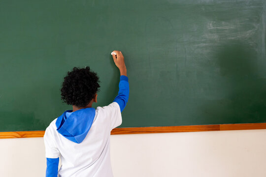 boy student writing on blank green chalkboard in classroom during lesson at school