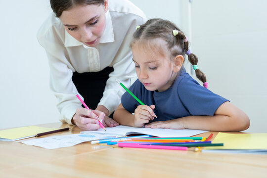 Teacher assisting young student with drawing and learning activity in classroom. Creative education, child development, personalized learning, and academic support concept.