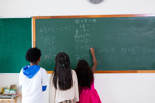 Boys and girls student writing on blank green chalkboard in classroom during lesson at school