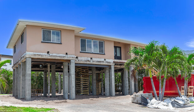 Coastal house renovation with structure elevated on concrete stilts and piles for flood protection on construction site