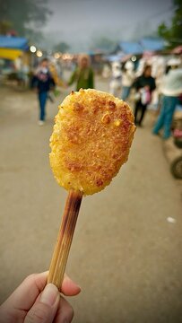 Hand holding Traditional Thai street food: Grilled sticky rice with egg (Khao Jee), served on bamboo skewers at a local Thai market