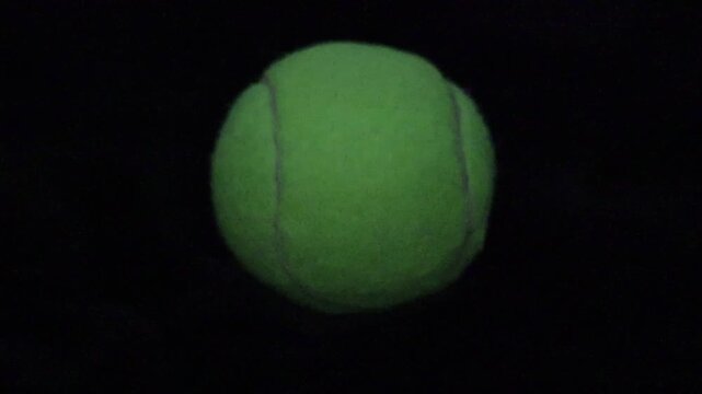 Una toma de cerca de una pelota de Tenis  con unas luces en un fondo negro