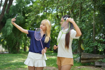 Obraz premium Two Asian Women Friends Taking Selfie on Phone to Update Social Media After Badminton .