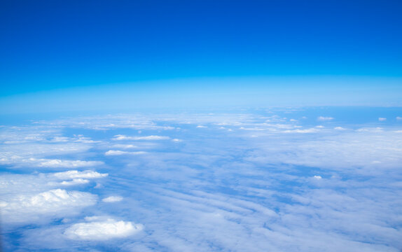 Beautiful aerial view of a cloud layer seen from an airplane at cruising altitude. Blue sky above and soft white clouds below create a peaceful atmosphere during a daytime flight.