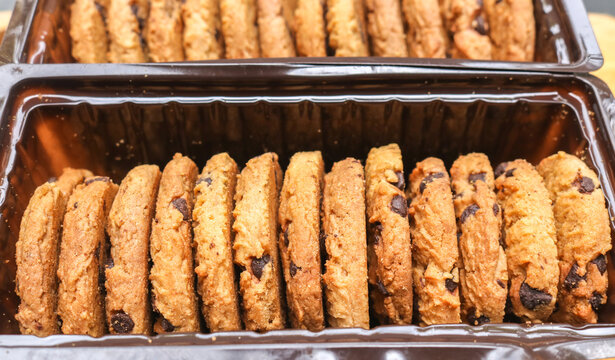 Close up of chocolate chip cookies in clear packaging. Golden brown, slightly crispy edges. Stacked neatly on a wooden cutting board
