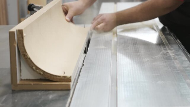 Furniture worker bending laminated plywood sheet on woodworking machine during furniture production process. Modern woodworking and manufacturing industry.
