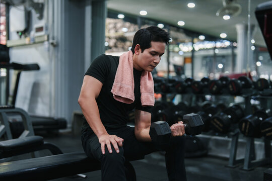 Asian man performing dumbbell bicep curl in gym for arm muscle workout fitness