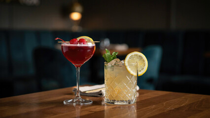 Two elegant colorful cocktails served in fancy glassware on a polished wooden bar top surface