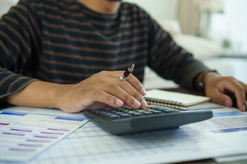 Fototapeta premium Person using a calculator with financial documents at home, concept of budgeting, expense planning, savings, and household money management.