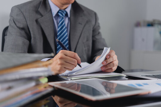Corporate executive reviewing stack of legal contracts holding pen auditing business paperwork checking compliance administration working at office desk for commercial corporate management