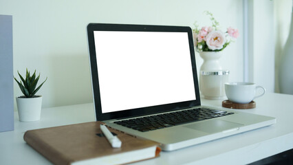 Fototapeta premium Laptop mockup with blank white screen on a clean desk, decorated with notebook, pen, plant, coffee cup, and flowers.