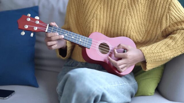 Asian woman in sweater playing ukulele in living room