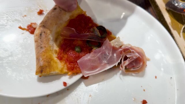 Close Up of Hand Picking Up Prosciutto Pizza Slice from Plate