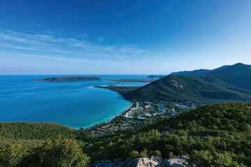 Fototapeta premium An expansive aerial view captures the stunning turquoise waters and lush green hills of a tropical coastline under a clear blue sky, showcasing nature's serene beauty.
