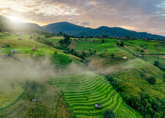 Obraz premium Landscape of rice terrace and hut with mountain range background and beautiful sunrise sky. Nature landscape. Green rice farm. Terraced rice fields. Travel destinations in Chiang Mai, Thailand.