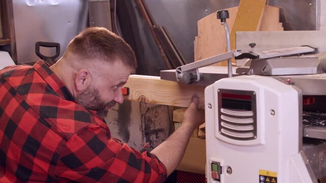 Carpenter occupation. Joinery equipment. Man starting lumber processing in furniture workshop pushing fastened together wood in thickness planer.