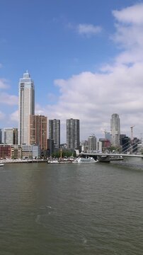 Aerial view of the modern skyline with skyscrapers and the Erasmusbrug bridge over the Nieuwe Maas river with boats on a sunny day, Rotterdam, Zuid-Holland, Netherlands.