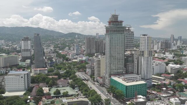 Aerial view of the modern urban skyline with high-rise buildings and lush green mountains under a cloudy sky Cebu City, Central Visayas, Philippines.