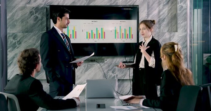 Asian female executive leading office meeting, explaining financial report with digital graph on screen, professional team listening and analyzing strategy for corporate business success