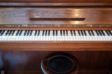 Close-up of an upright wooden piano keyboard with a round piano stool. Classical musical instrument interior detail with vintage wood texture and copy space.  © Marek
