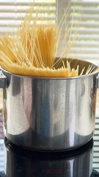The spaghetti noodles are being added to the pot of boiling water.