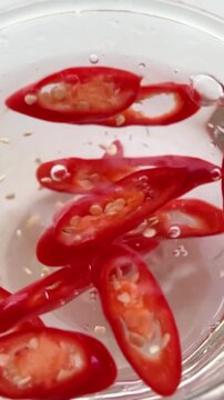 Sliced ​​red chili peppers are being tossed into the water in the glass.