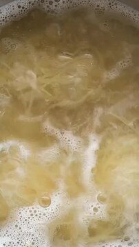 The spaghetti noodles are boiling in water.
