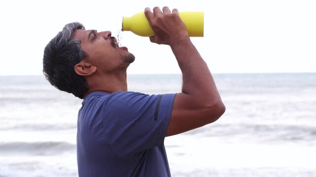 Man Drinking Water from Yellow Bottle on Beach After Summer Workout for Hydration Lifestyle