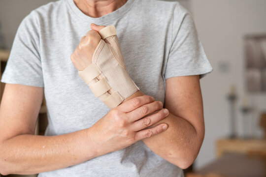 Woman experiencing wrist joint pain and discomfort, wearing a therapeutic wrist brace for support and immobilization due to tendinitis or rhizarthrosis