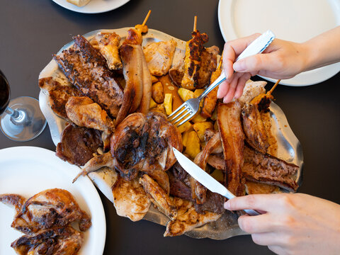 Quails cooked on the grill and served on a large plate, against the background of female hands with with cutlery