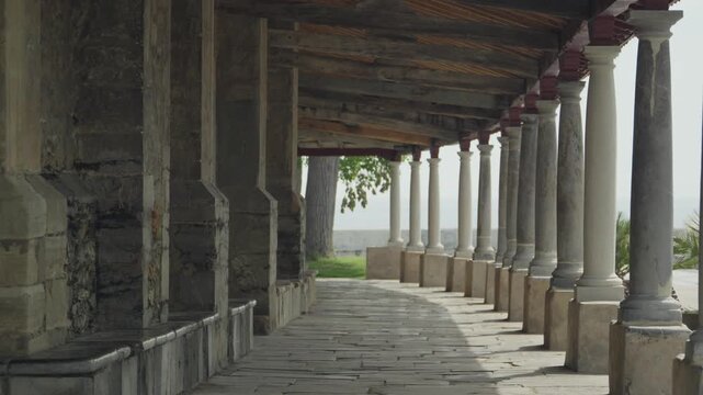 Historic stone colonnade with white columns and wooden roof beams at Iglesia de Santa Maria de Luanco.
