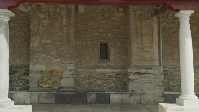 Framing weathered stone wall of historic church between white columns.
